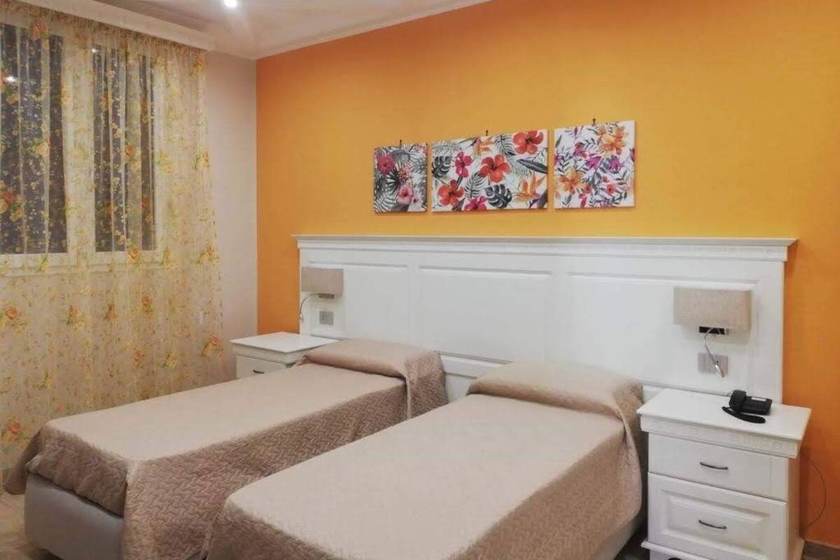 Ein Hotelzimmer mit zwei Betten, einem weißen Kopfstützenverkleidung, einem kleinen Nachttisch mit Lampe und einem an der Wand montierten Telefon.