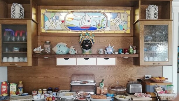 A kitchen with wooden cabinets, a stained glass window above the sink, and various kitchen items on the counter. - Stella del Mare (Licata)