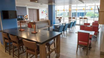 A modern restaurant with a long communal table, individual booths, and a bar area.