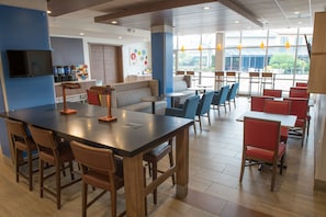 A modern restaurant with a long communal table, individual booths, and a bar area.