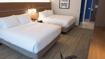 A hotel room with two beds, a nightstand, a lamp, a framed picture on the wall, and a door leading to another room.
