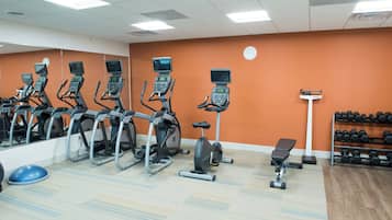 Ein Fitnessraum mit mehreren Ergometer, einem Laufband und einer Bank.