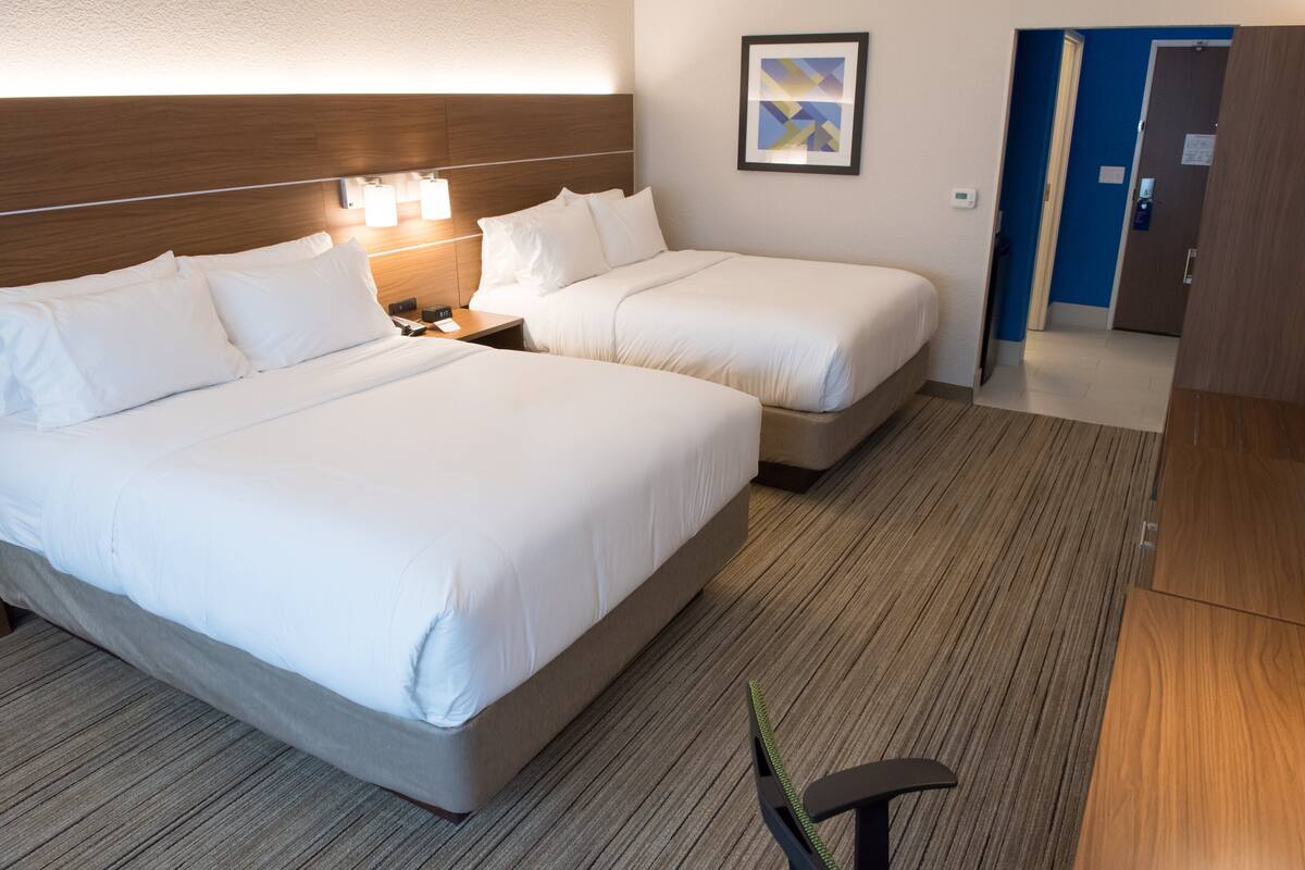 A hotel room with two beds, a nightstand, a lamp, and a framed picture on the wall.