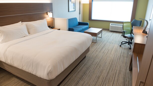 A hotel room with a large bed, a blue sofa, a small table, and a desk with a chair.