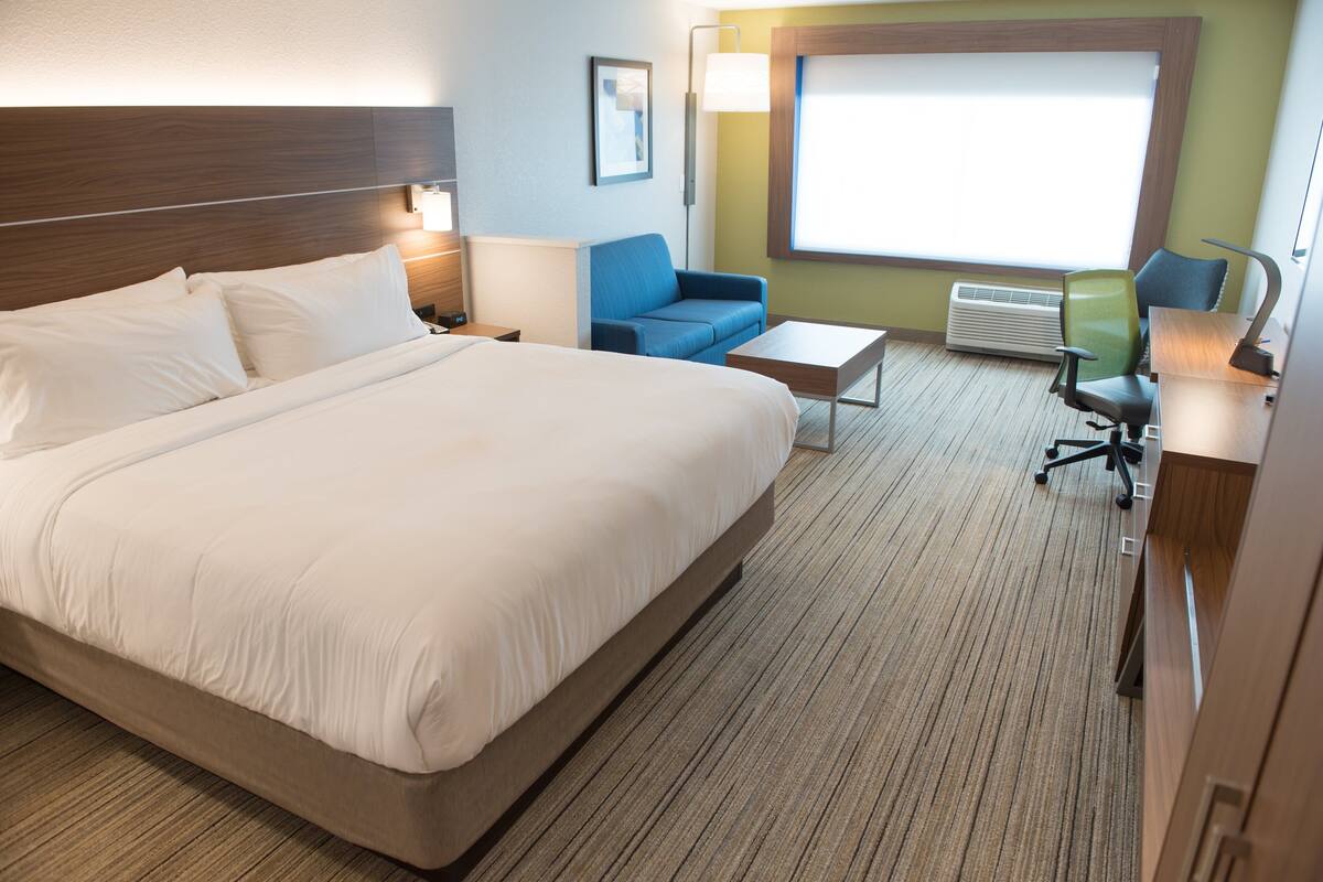 A hotel room with a large bed, a blue sofa, a small table, and a desk with a chair.