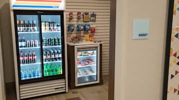A vending machine with various beverages and snacks, a small refrigerator with frozen items, and a sign indicating a market area.