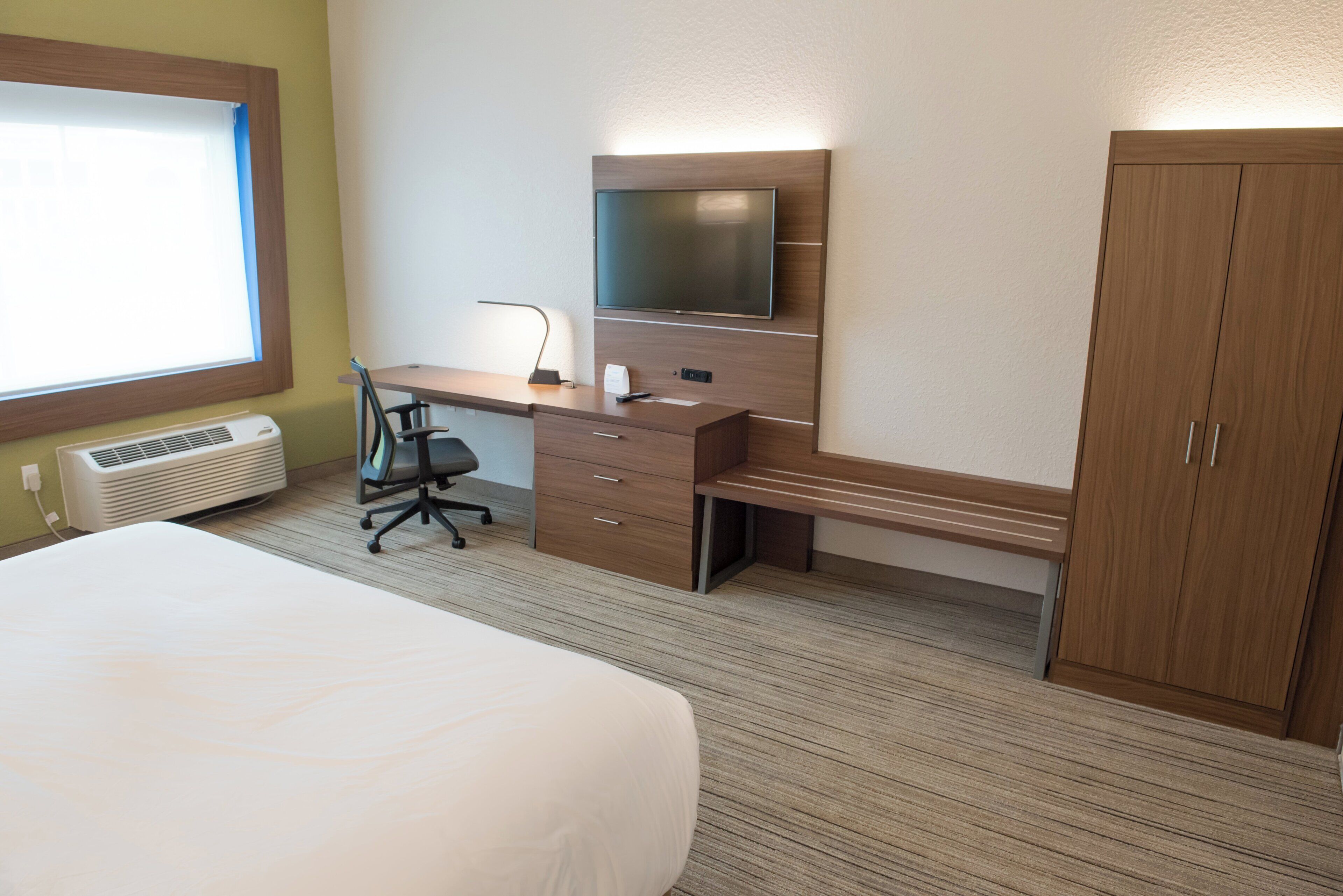 Habitación de hotel con una cama, un escritorio con silla, un televisor y un armario.