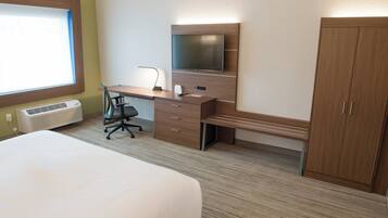 Habitación de hotel con una cama, un escritorio con silla, un televisor y un armario.