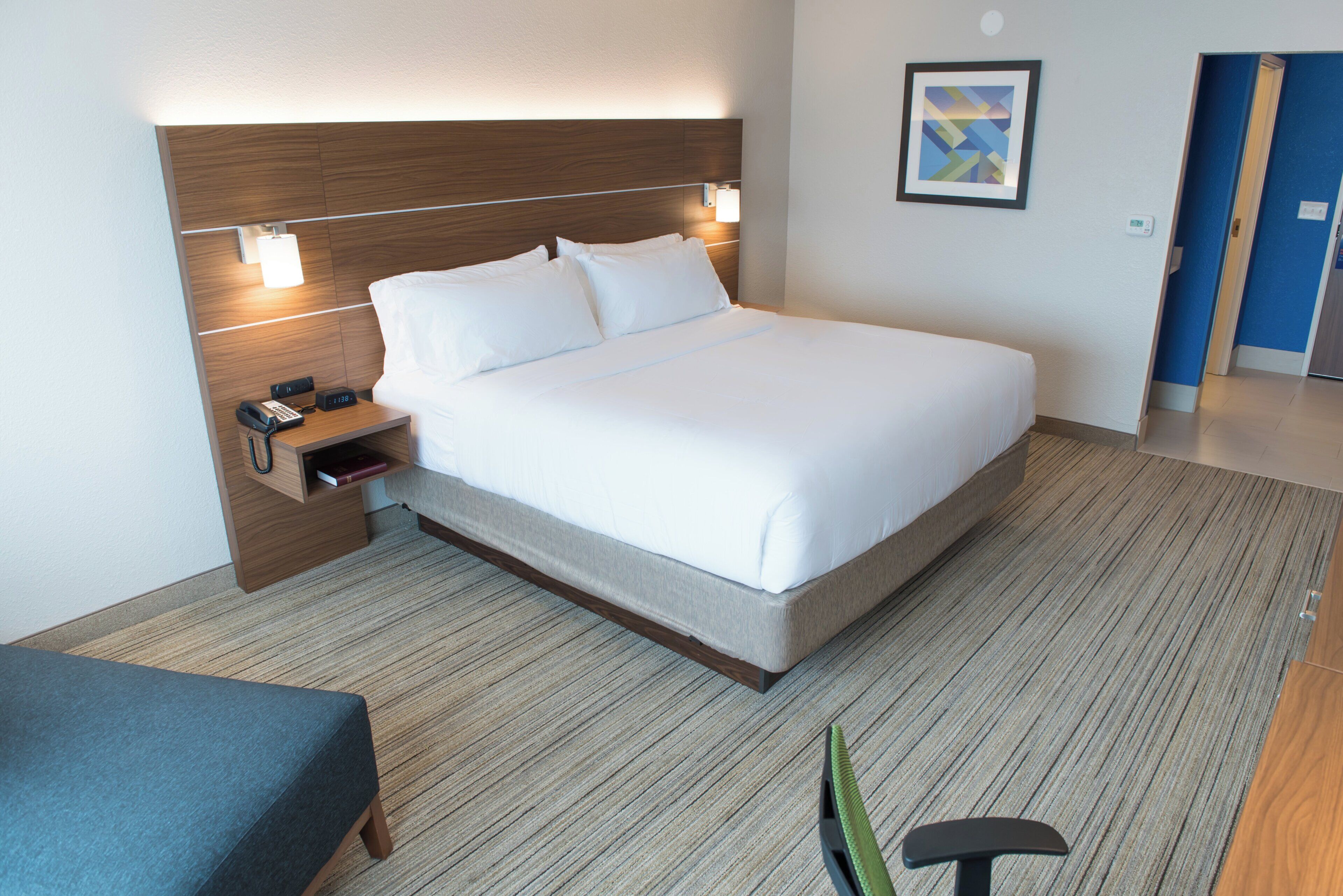 Habitación de hotel con una cama grande, mesita de noche con teléfono y un pequeño rincón para leer.
