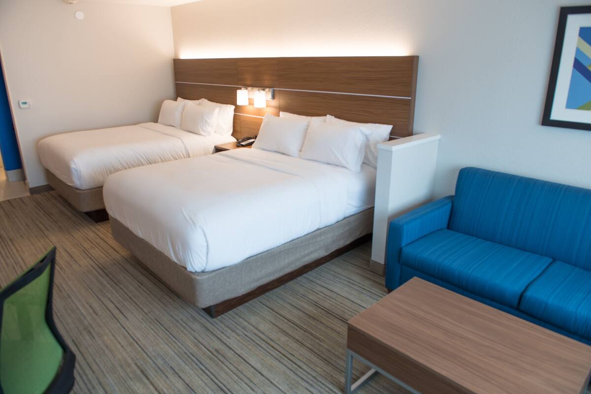 A hotel room with two beds, a blue sofa, a wooden table, and a nightstand with a lamp.