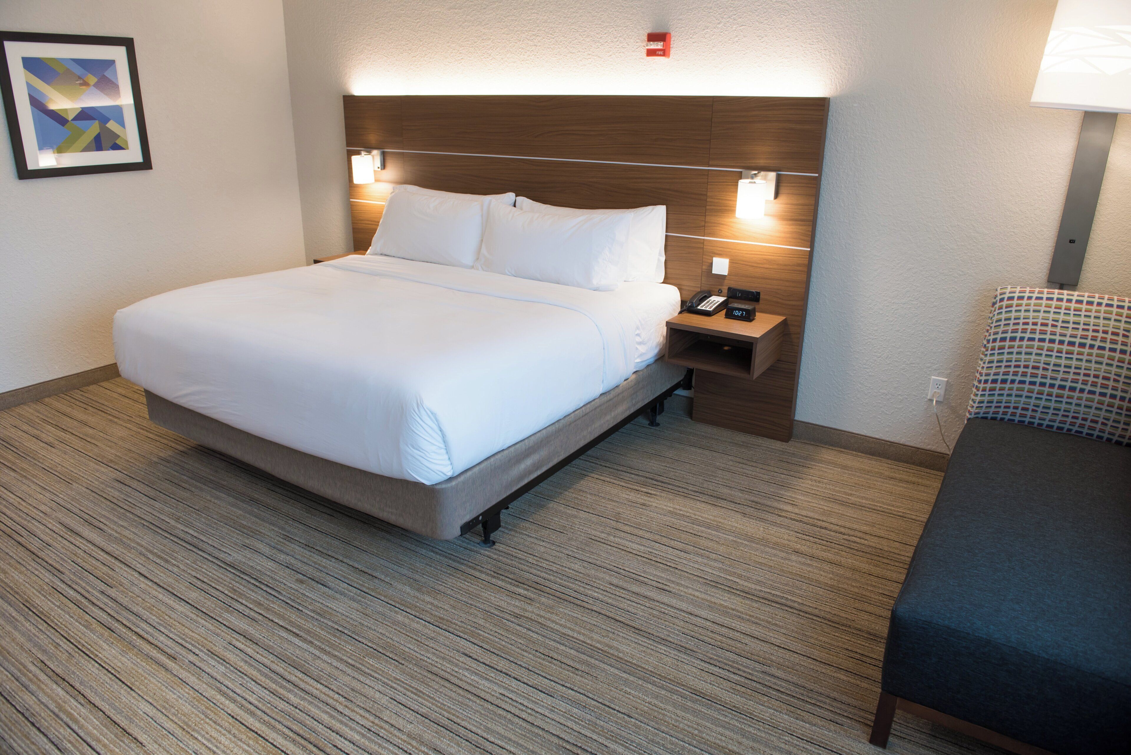 Una habitación de hotel con cama, mesita de noche y una silla.