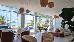 A spacious lobby with modern furniture, large windows offering a view of the sea and parked cars.