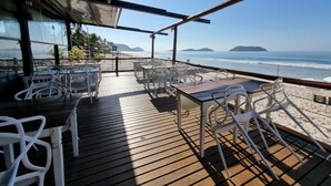 An outdoor seating area with tables and chairs, overlooking a beach and ocean.