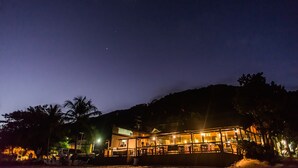 A building with a glass facade, surrounded by palm trees and a mountainous backdrop.