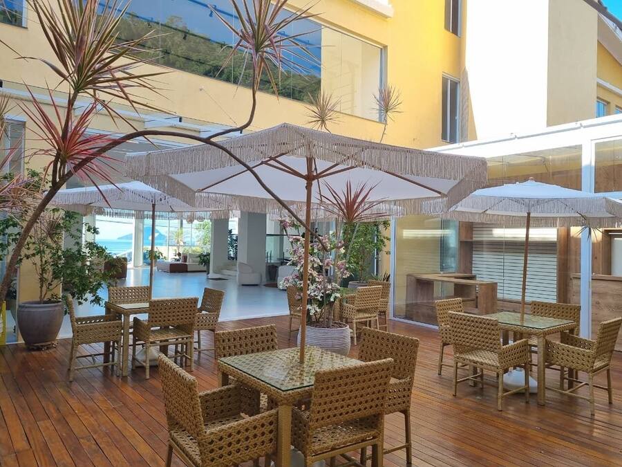 Eine Terrasse im Freien mit Korbmöbeln und Sonnenschirmen, umgeben von Pflanzkübeln und Blick auf das Meer.