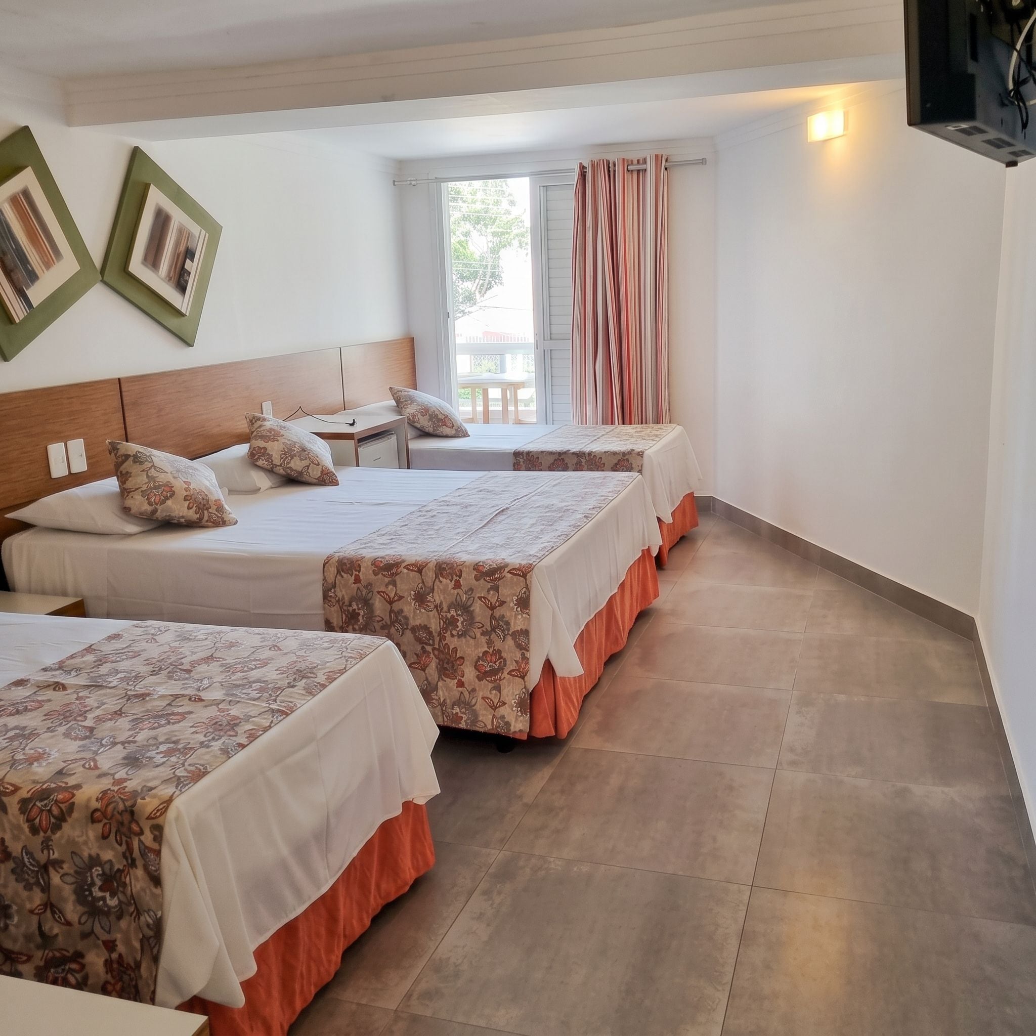 Une chambre d’hôtel avec trois lits, une tête de lit en bois, une fenêtre avec des rideaux et une vue sur l’extérieur.