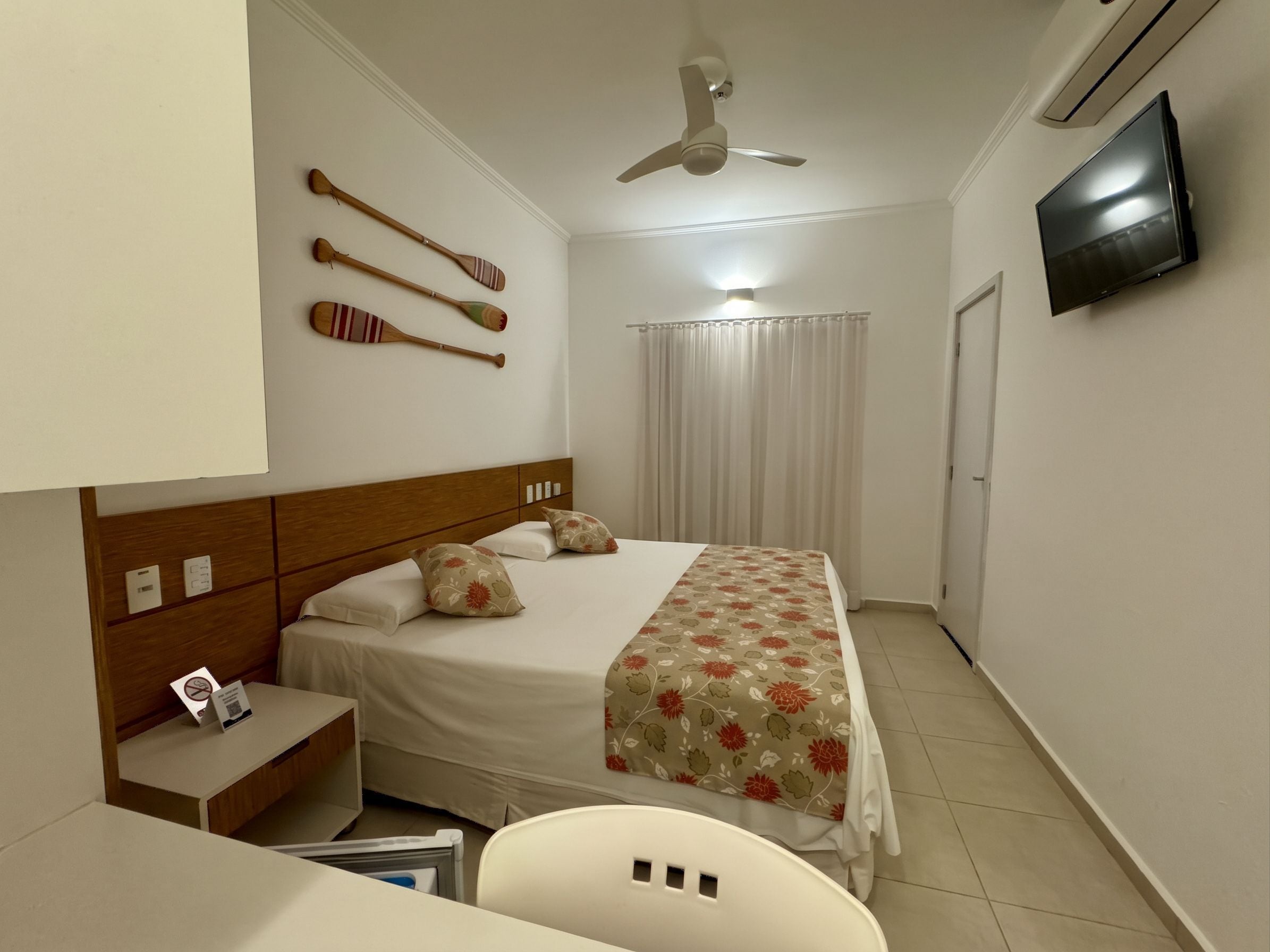 Une chambre d’hôtel équipée d’un lit, d’un bureau, d’une chaise, d’un ventilateur de plafond et d’un téléviseur fixé au mur.