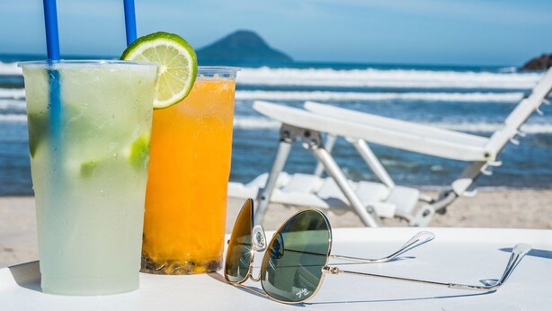 Two drinks on a table with a pair of sunglasses and beach chairs in the background.