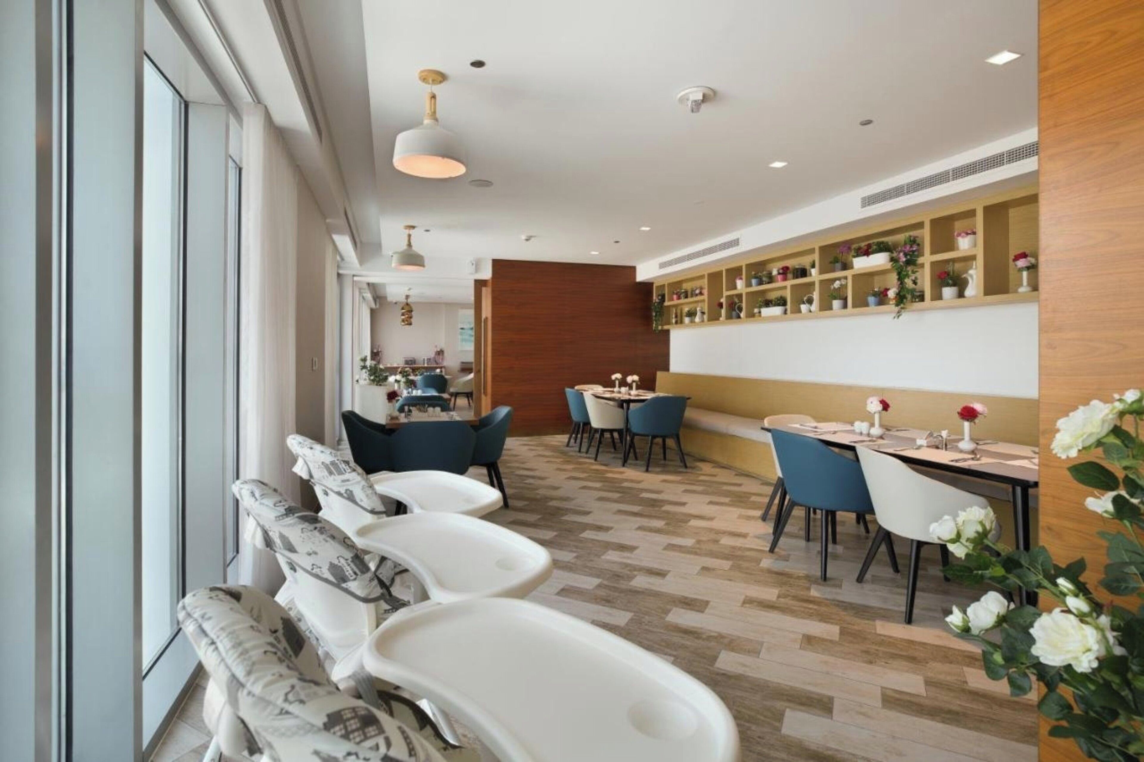 A modern restaurant with a long counter, white chairs, and a wooden wall with shelves.