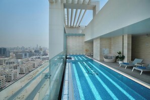 Una piscina a sfioro sul tetto con vista sulla città, sedie a sdraio e un pergolato.