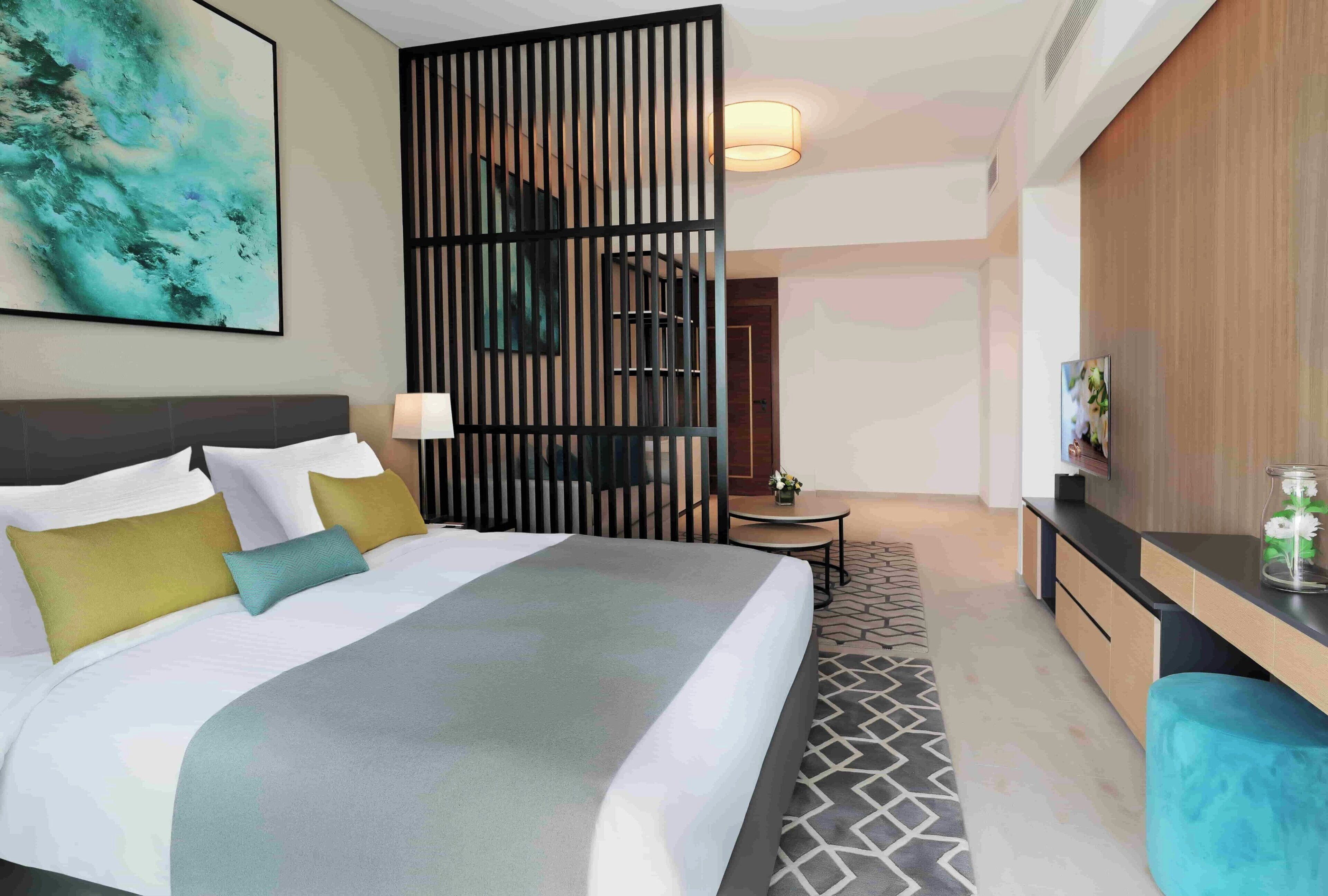 Une chambre d’hôtel moderne équipée d’un grand lit, d’un bureau, d’une chaise et d’un paravent décoratif.