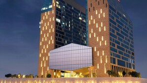 Un hôtel moderne à la façade géométrique originale, caractérisée par des lignes verticales illuminées et une structure en verre imposante au centre.