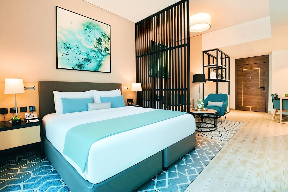 Ein modernes Hotelzimmer mit einem großen Bett, einem Schreibtisch mit Stuhl, einem Bücherregal und einer dekorativen Wandverkleidung.