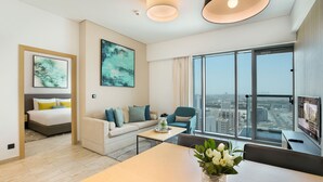 Une chambre d’hôtel moderne équipée d’un lit, d’un canapé, d’une table à manger et d’une grande fenêtre donnant sur la ville.
