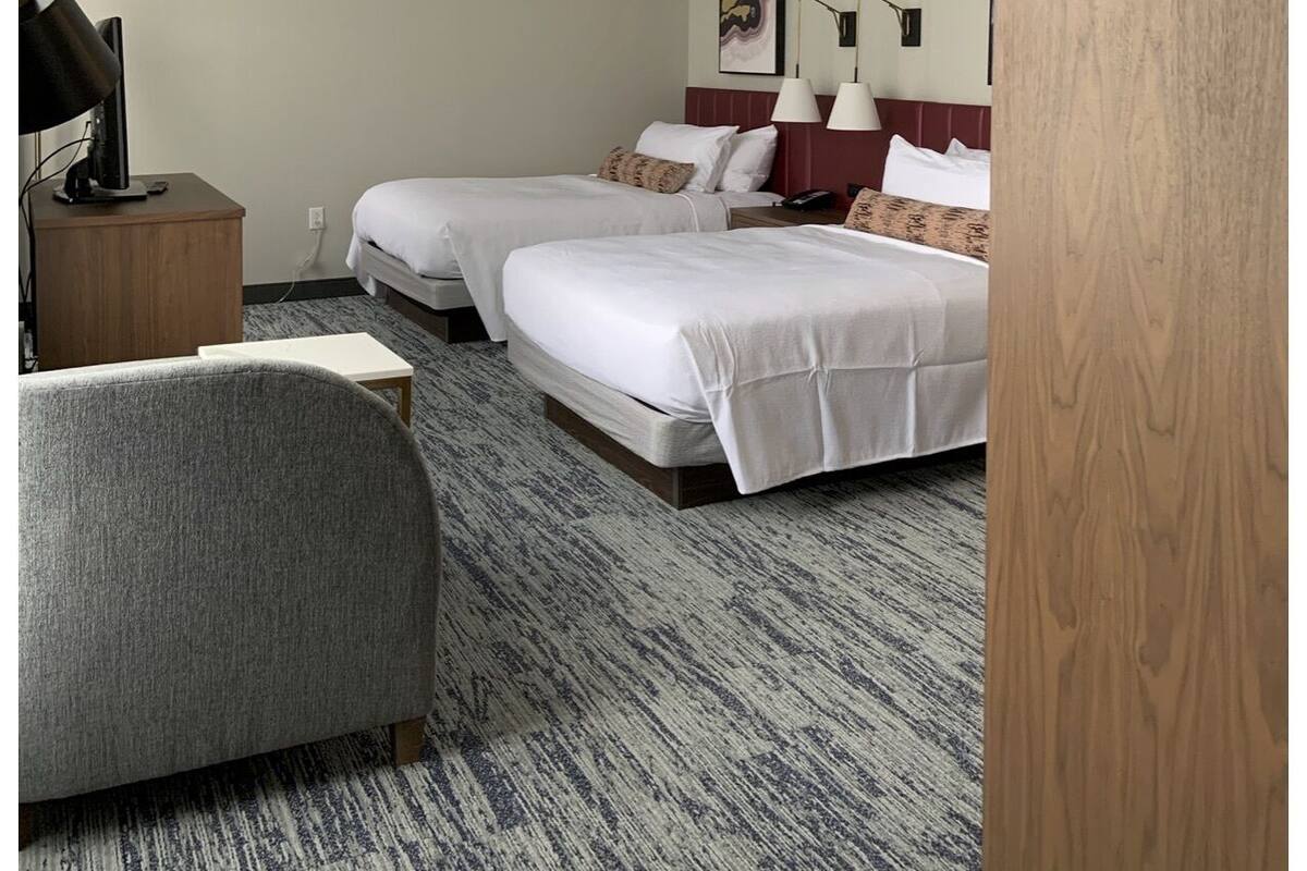 A hotel room with two beds, a desk, a chair, and a wooden door.