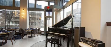 Una habitación amplia con un piano de cola, una pequeña mesa y sillas dispuestas alrededor de un espacio central.