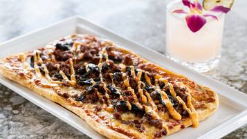 Une assiette rectangulaire contenant une pizza garnie de divers ingrédients, accompagnée d’une boisson décorée.