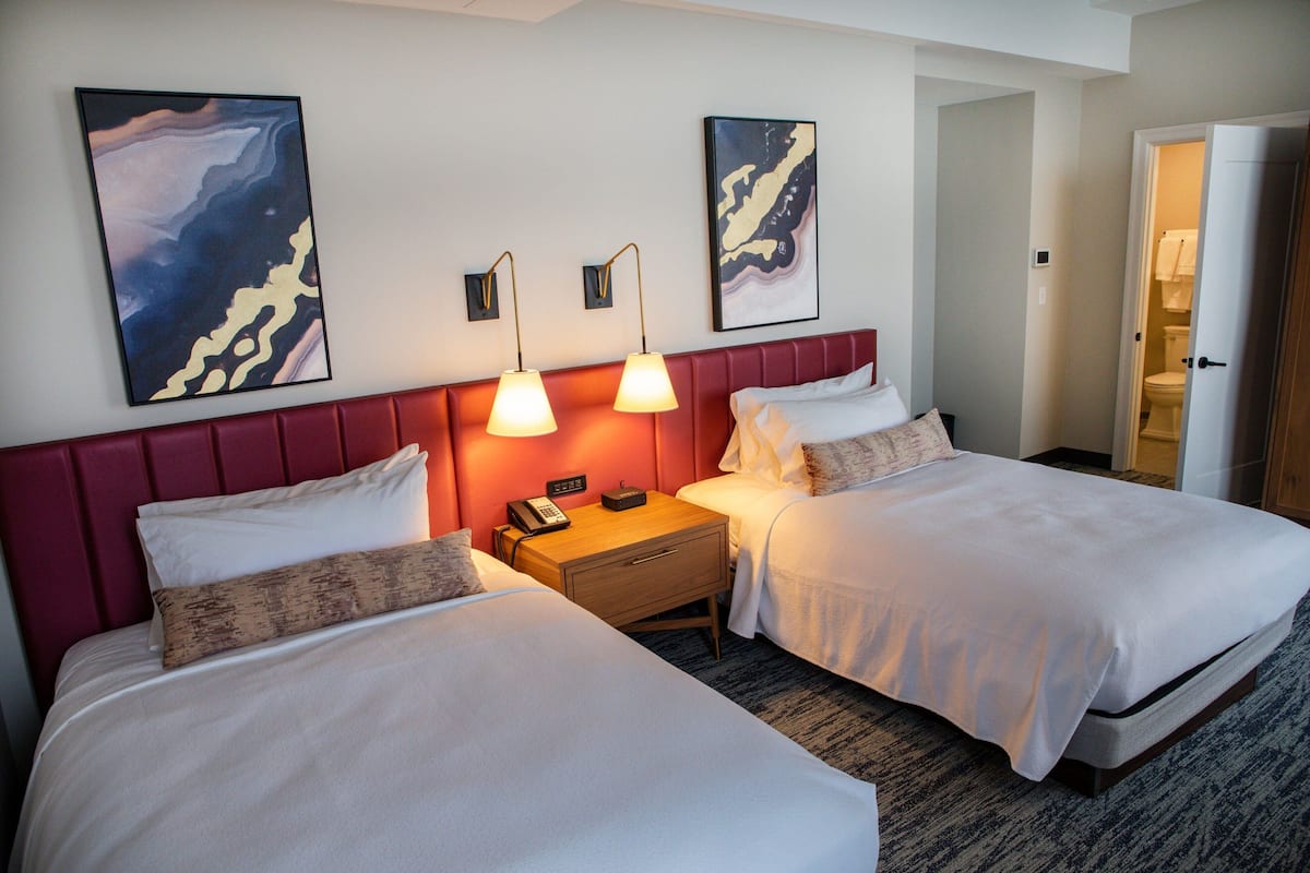 A hotel room with two beds, a nightstand, and two wall-mounted lamps.