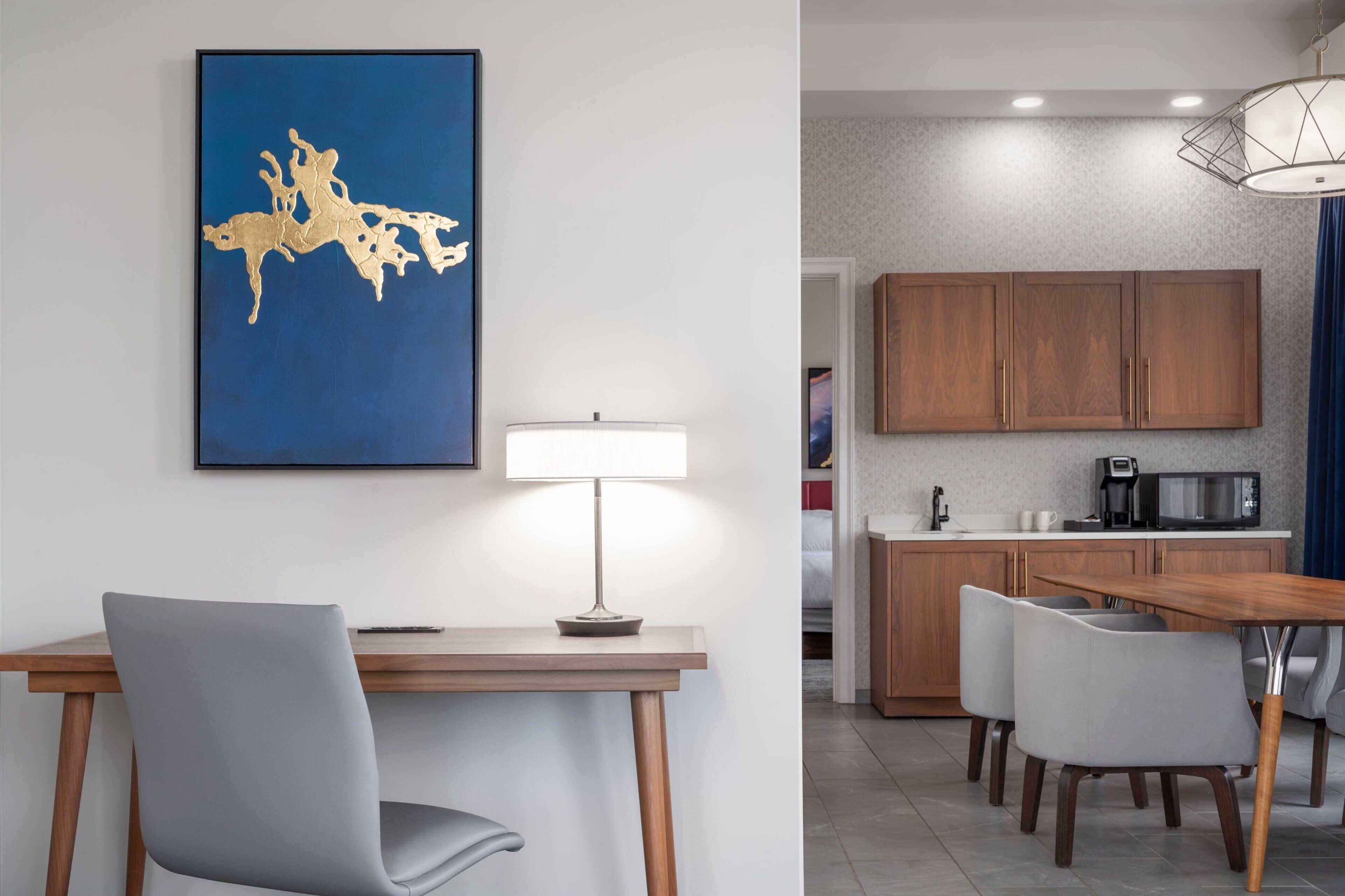A modern kitchen with wooden cabinets, a dining area with a table and chairs, and a blue wall with a gold abstract painting.