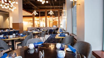 A modern dining area with multiple tables and chairs, overhead lighting, and a view of the interior space.