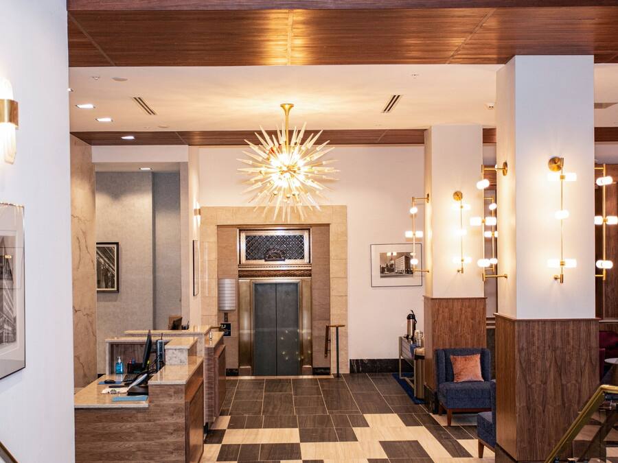 A lobby with a reception desk, a large chandelier, and a staircase leading to an upper level.