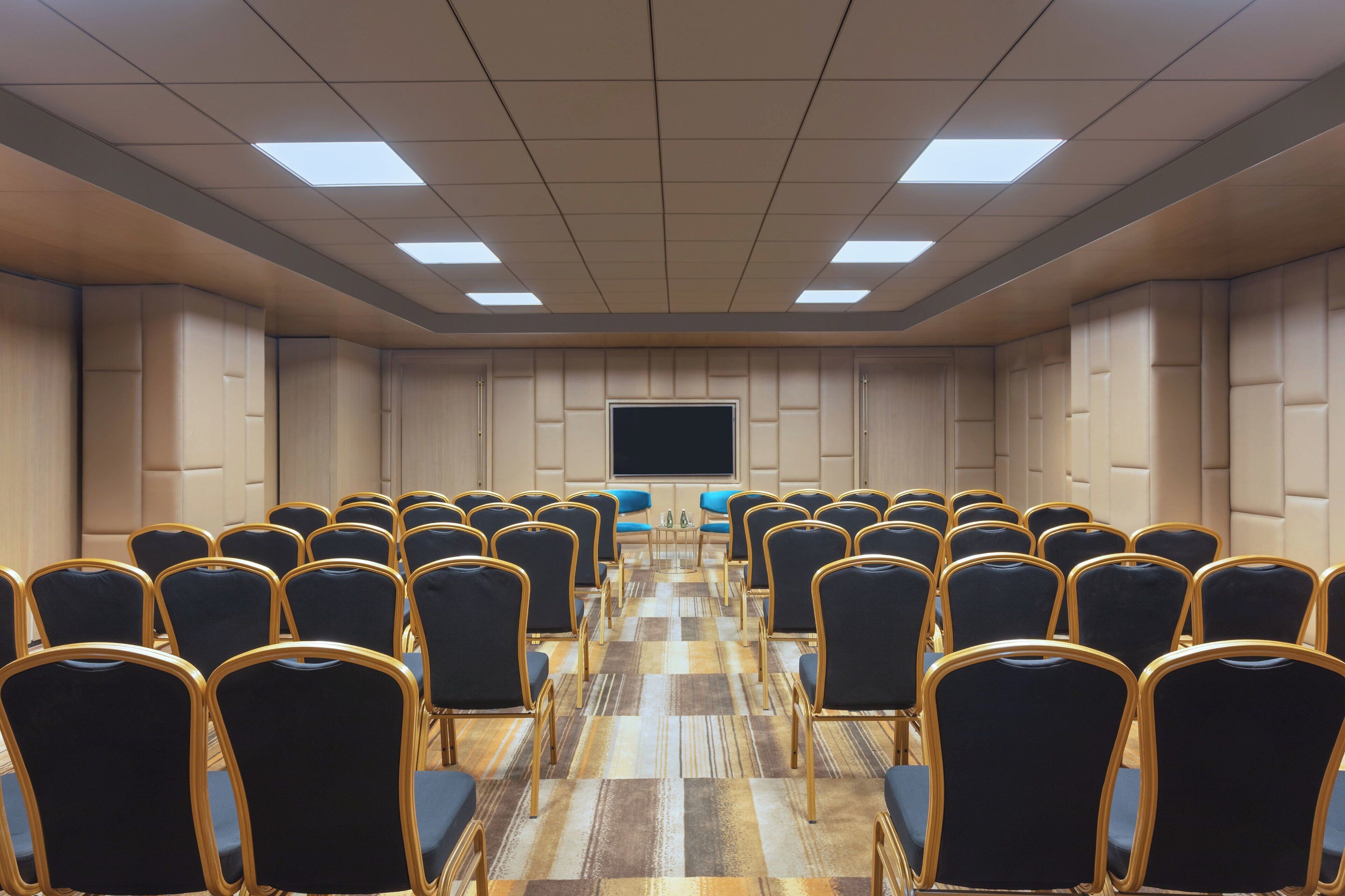 A conference room with rows of chairs, a large screen, and a patterned carpet.