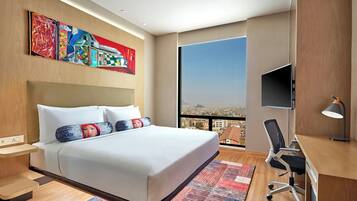 Un hotel moderno con una cama grande, un escritorio con una silla, televisión y vistas a la ciudad por la ventana.