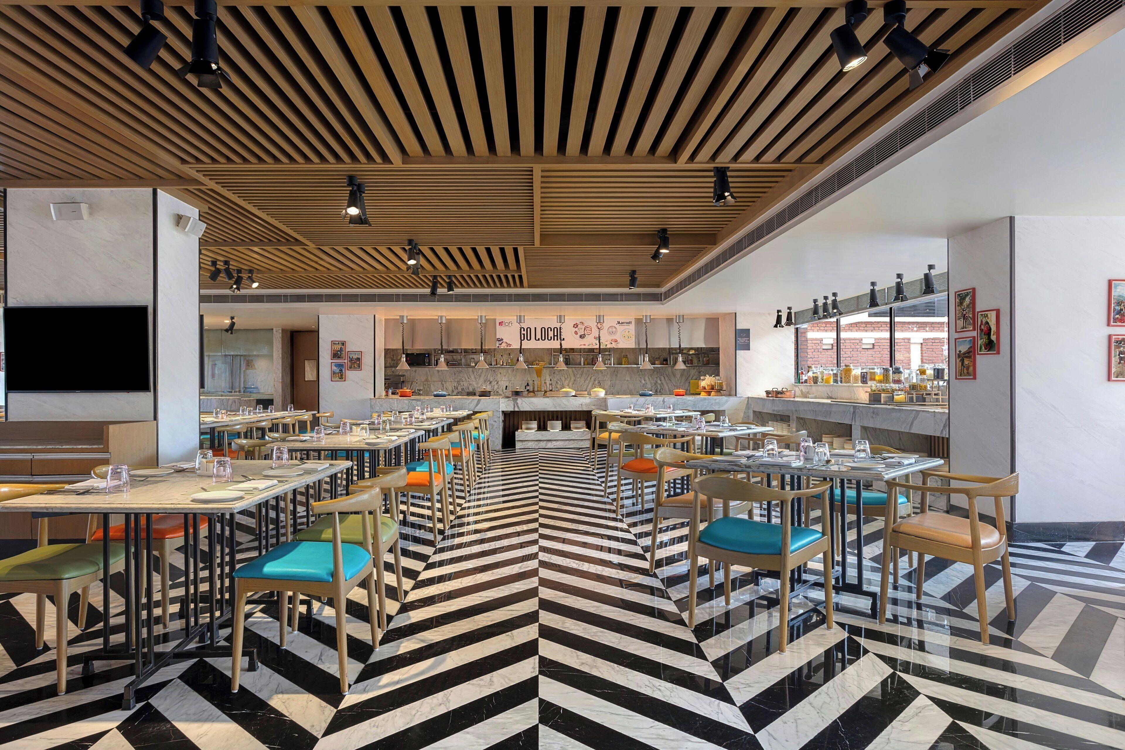 A modern restaurant with a black and white striped floor, wooden ceiling, and a variety of seating options.