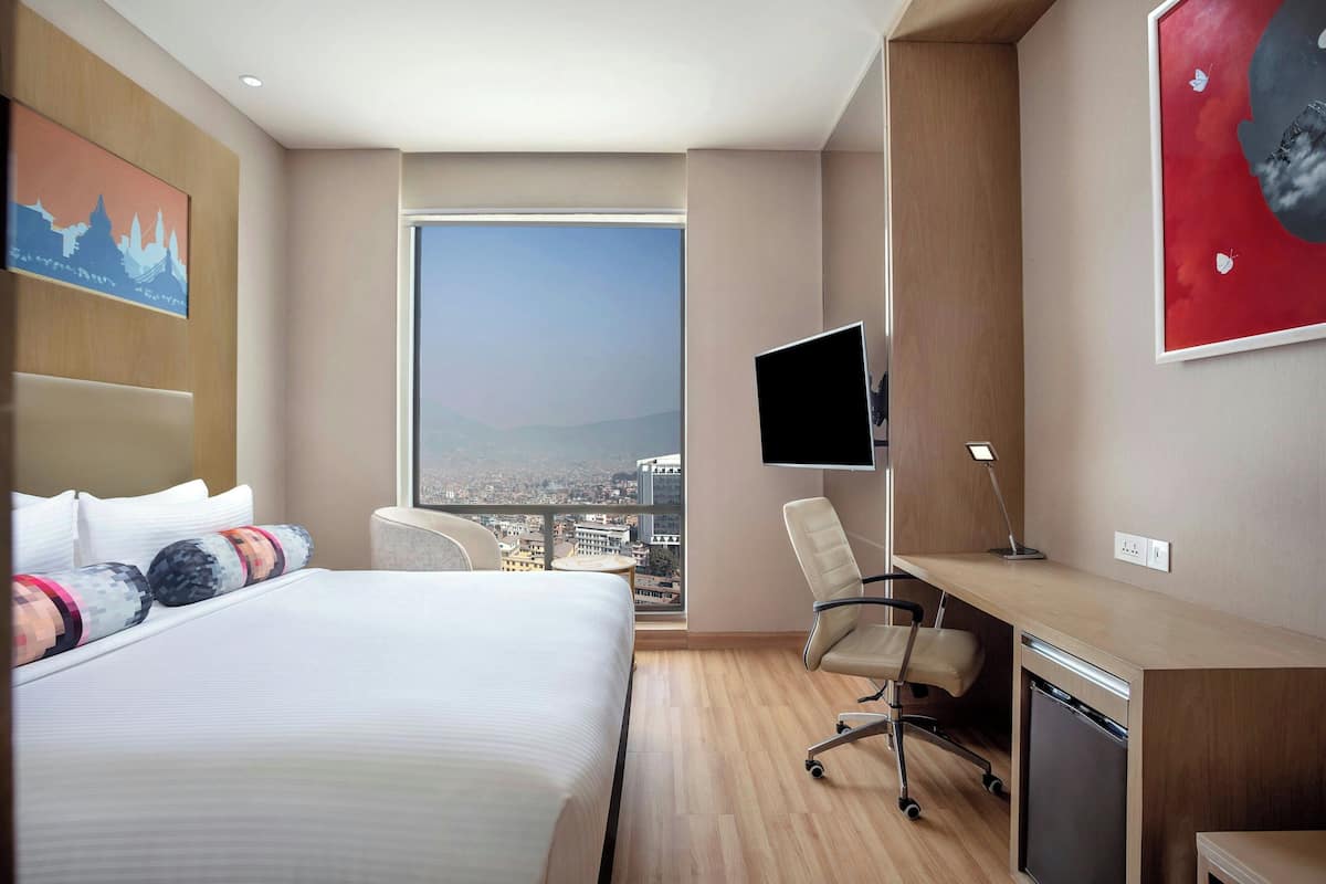 Une chambre d’hôtel équipée d’un lit, d’un bureau, d’une chaise et d’une grande fenêtre donnant sur la ville.