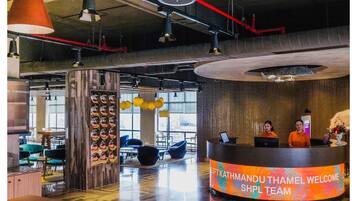A modern reception area with a digital welcome screen, a wooden reception desk, and a seating area with chairs and tables.