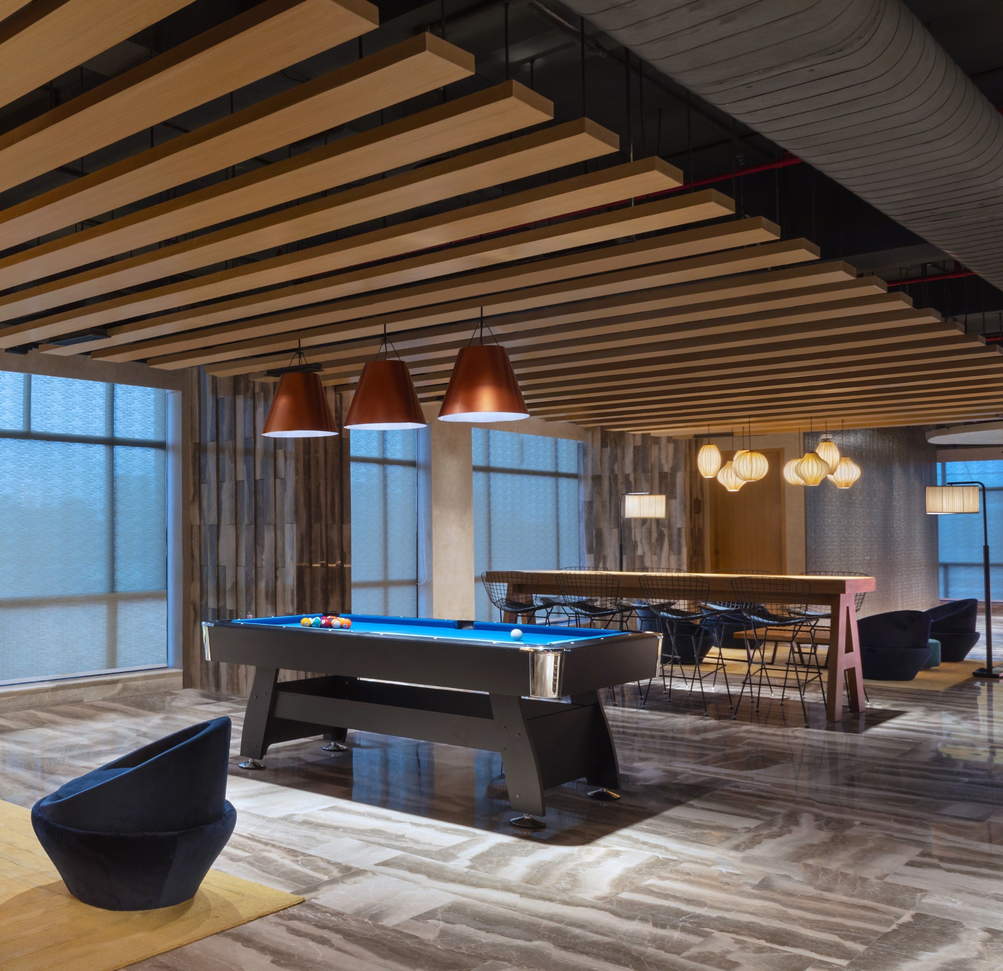 Un espace moderne dédié aux tables de billard, situé à l’intérieur, avec une table de billard entourée de chaises et de tables, et une grande fenêtre qui laisse entrer la lumière naturelle.