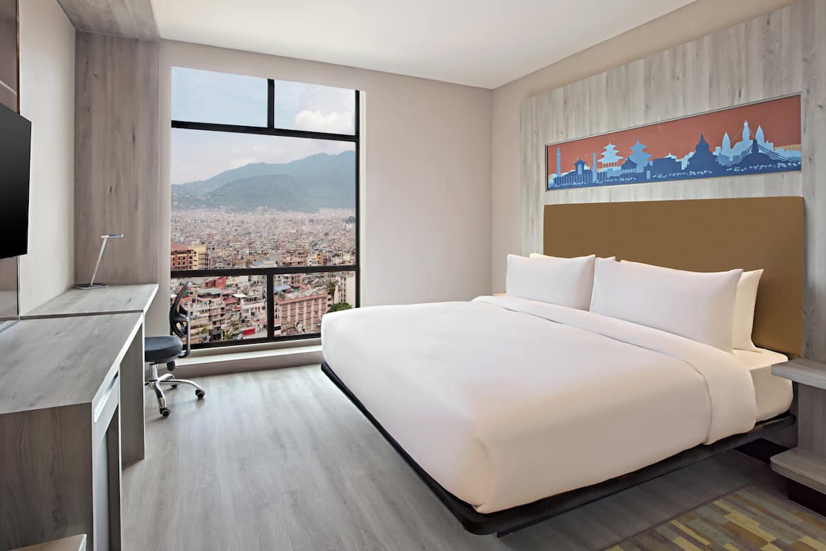 Une chambre d’hôtel moderne dotée d’un grand lit, d’un bureau et offrant une vue sur le paysage urbain grâce à une grande fenêtre.