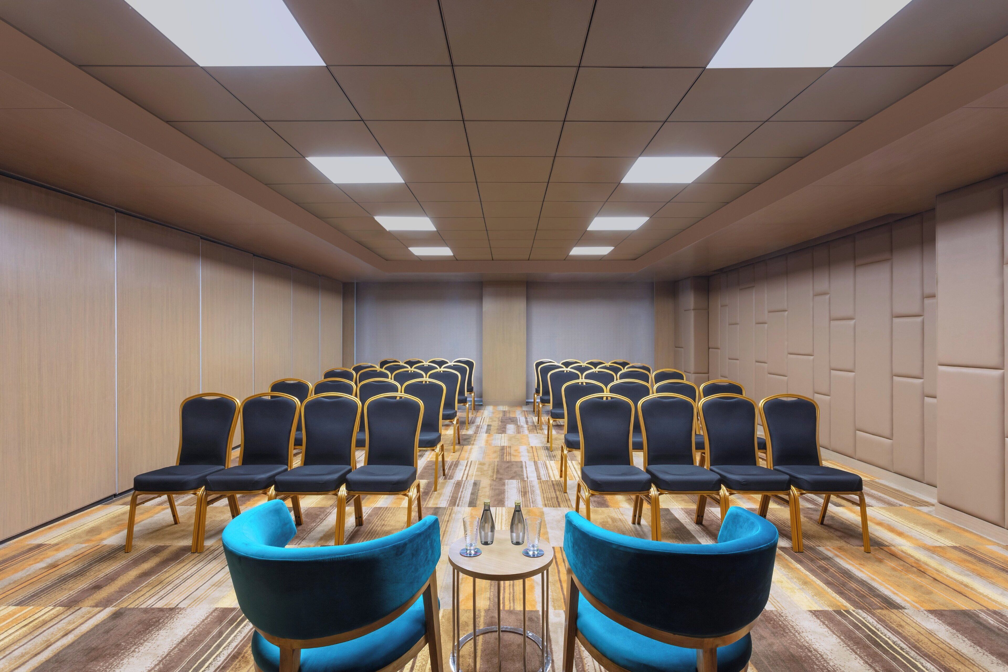 Konferenssihuone, jossa on riveissä tuoleja, puulattia ja valaistu katto.