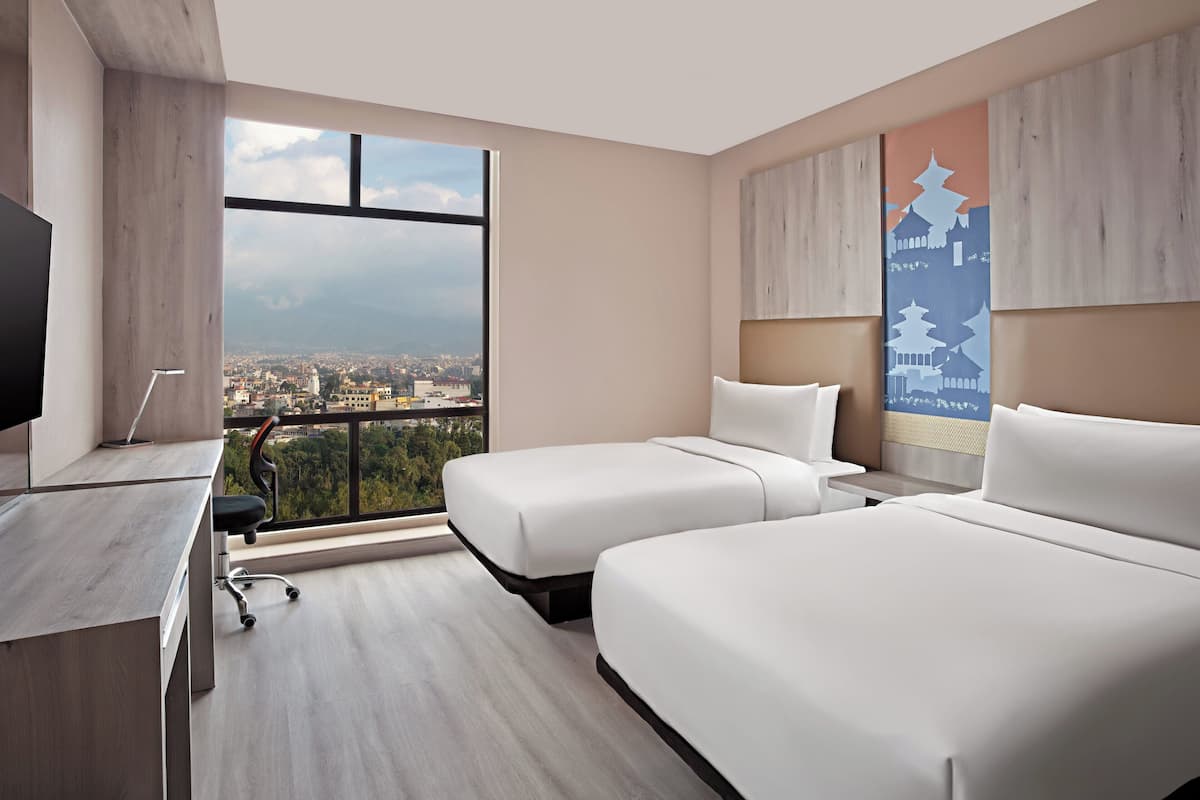 Une chambre d’hôtel avec deux lits, un bureau et une grande fenêtre donnant sur la ville.