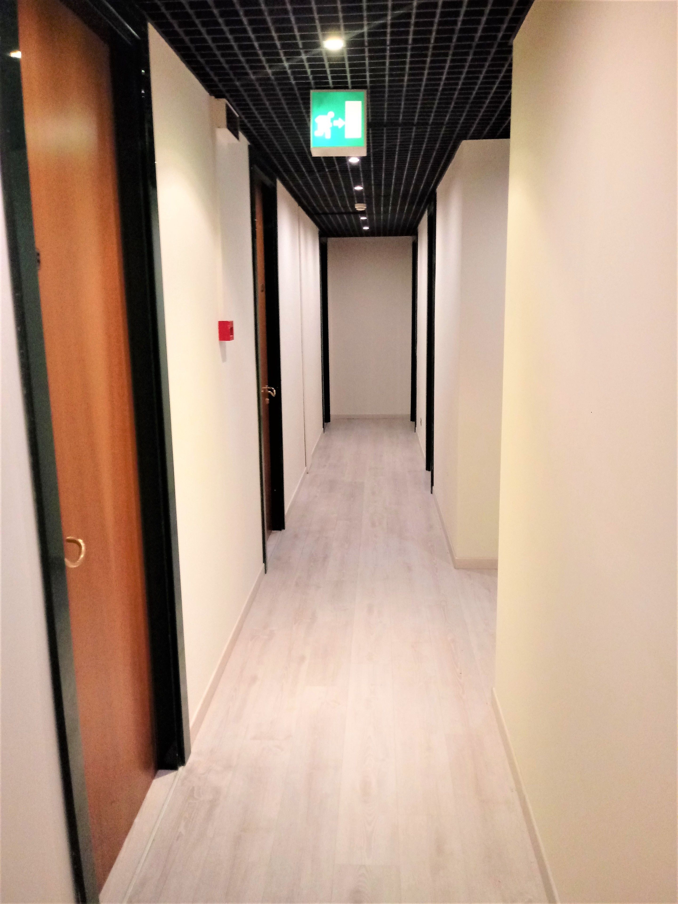A hallway with wooden doors, a light-colored floor, and a ceiling with a grid pattern.