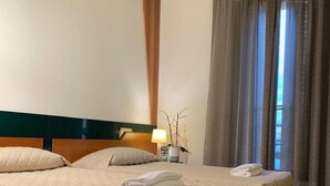 A hotel room with two beds, a nightstand, a lamp, and a window with curtains. - Hotel Dozza (Dozza)