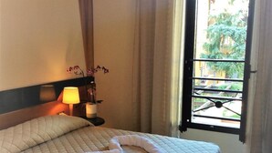 A neatly made bed with a quilted cover, a bedside lamp, and a vase with flowers on the nightstand. - Hotel Dozza (Dozza)