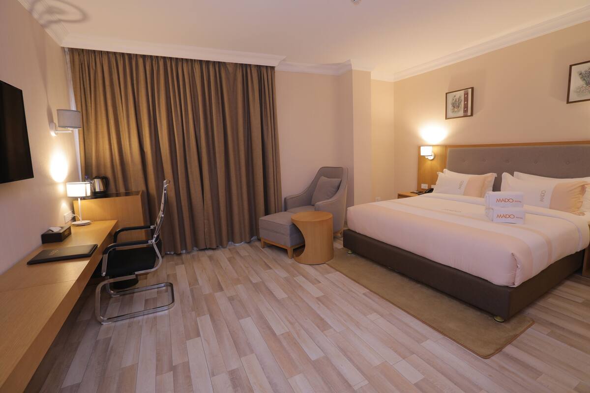 Una habitación de hotel con una cama, un escritorio, una silla, un televisor y un ventanal con cortinas.