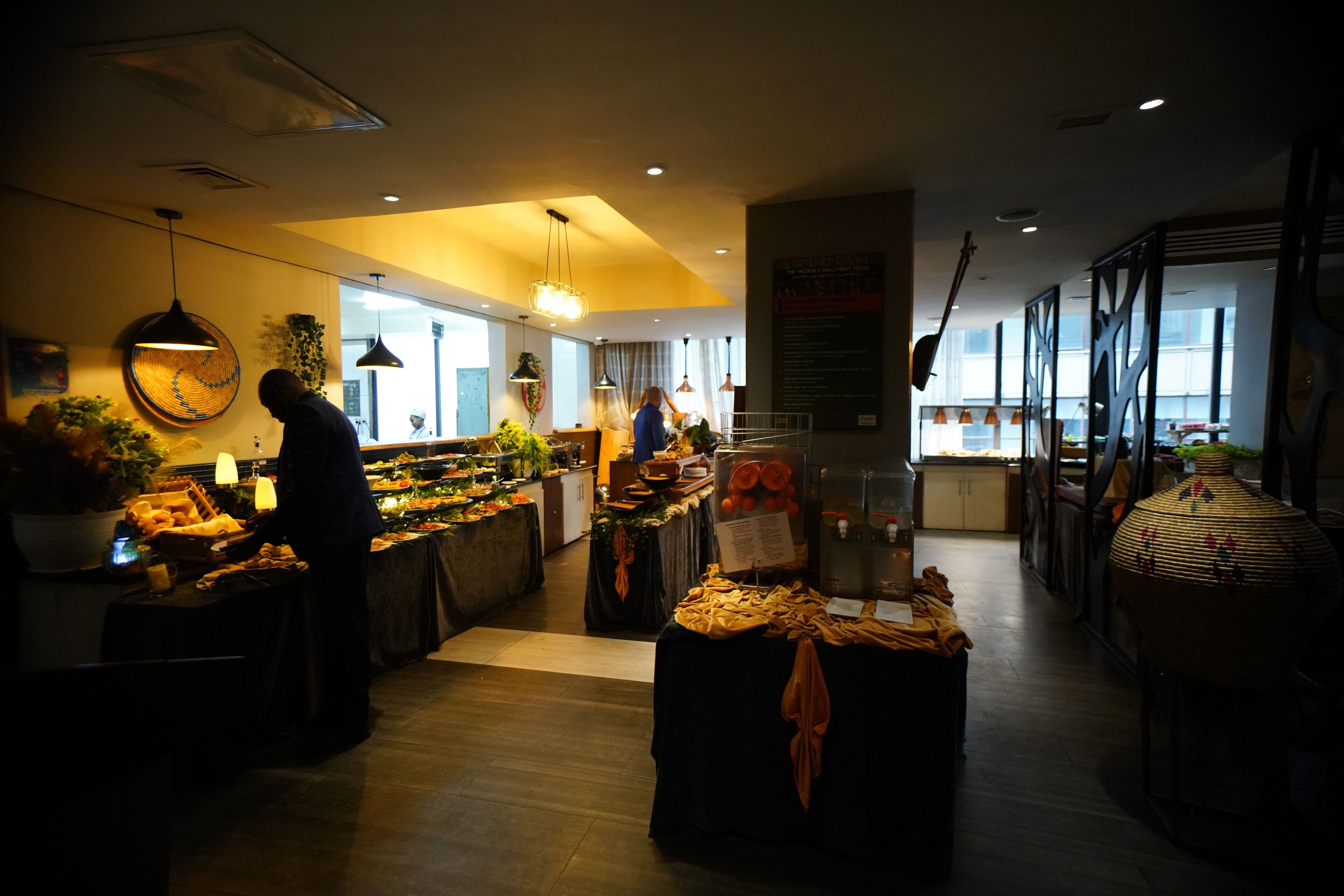 A modern restaurant with a central island, ambient lighting, and a view of the city through large windows.