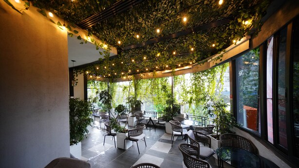Un patio interior con mesas y sillas, rodeado de grandes ventanales y follaje.
